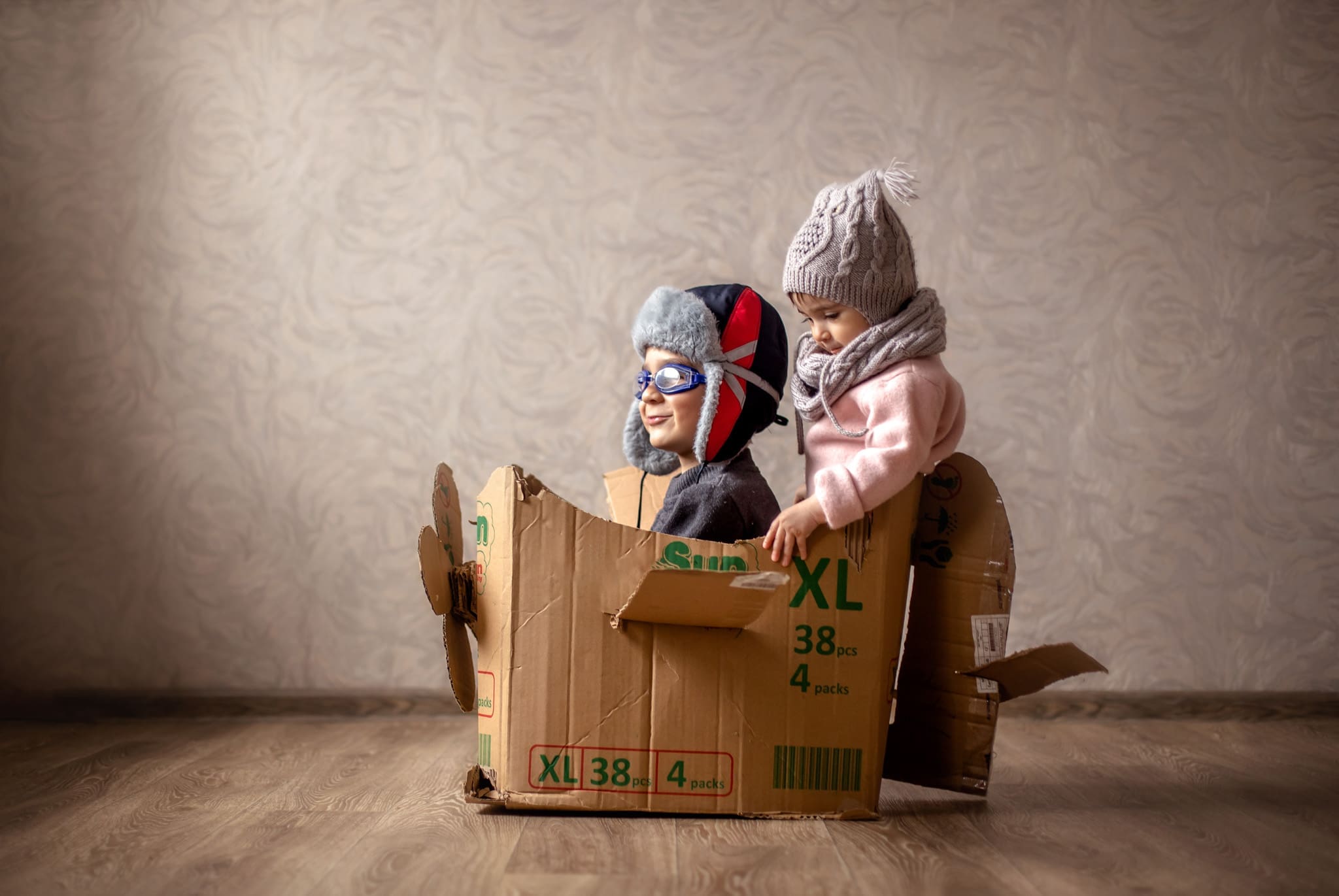 Two young children enjoy pretend play in a cardboard airplane, illustrating creative play to help with moving transition.