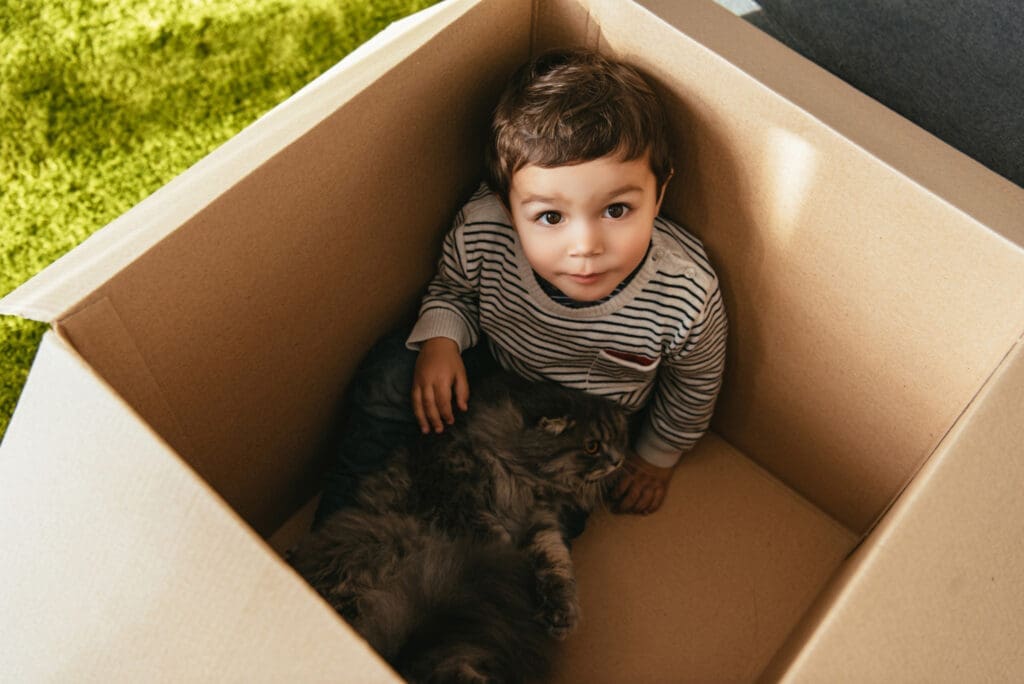 Young child and their fluffy cat sitting together inside a moving box, symbolizing comfort during the transition to a new home.