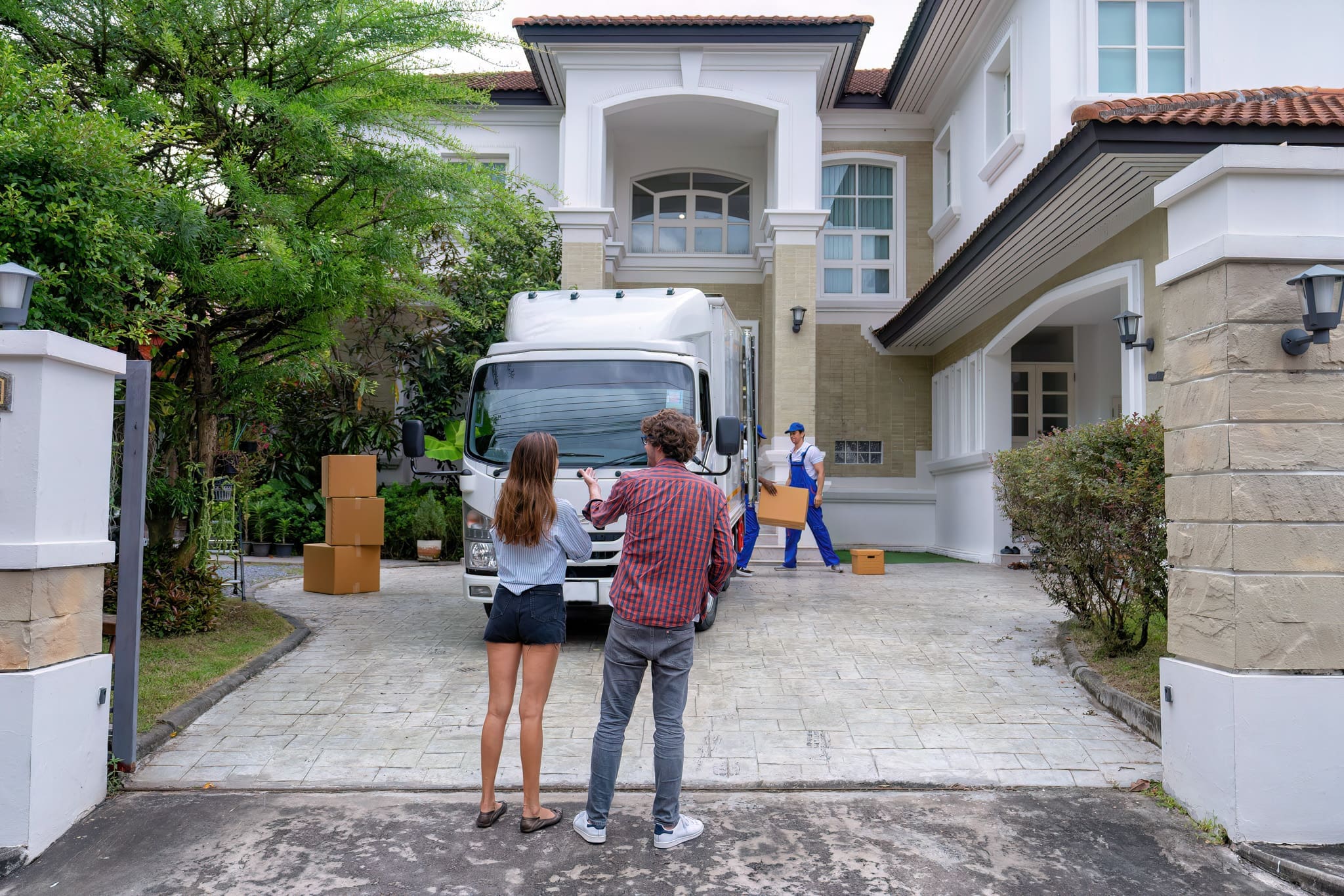 Young couple excitedly holding a cardboard box and home essentials while entering their new house.