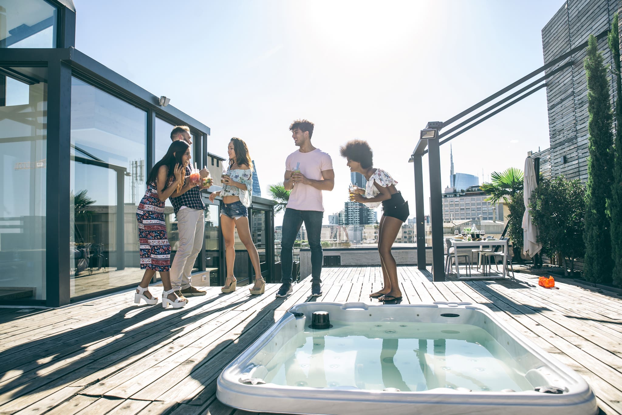 Group of friends enjoying a rooftop party beside an empty hot tub with city skyline in the background.